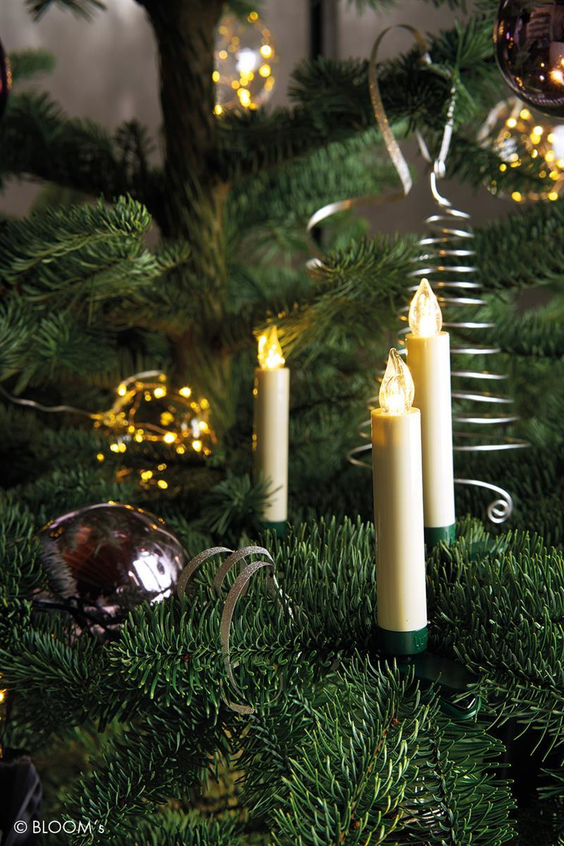 Beleuchtete Weihnachtskerzen auf tannengrünem Hintergrund mit Christbaumkugeln und Lichterketten.