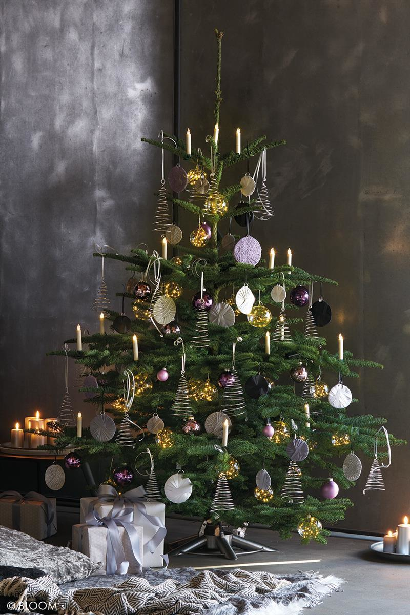 Ein geschmückter Weihnachtsbaum mit Lichtern, Kugeln und Kerzen vor einer dunklen Wand mit Geschenken.