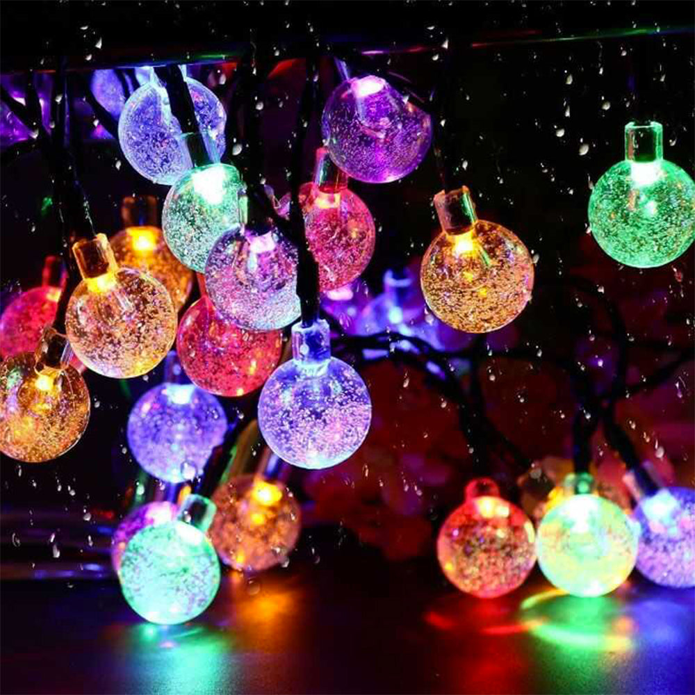 Bunte, leuchtende Glaskugeln einer Lichterkette glitzern in der Dunkelheit vor einem dunklen Hintergrund.
