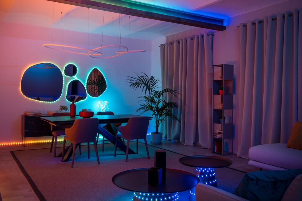 Moderne woonkamer met eethoek, blauw-rode LED-verlichting, ronde tafels, planten en spiegels aan de muur.