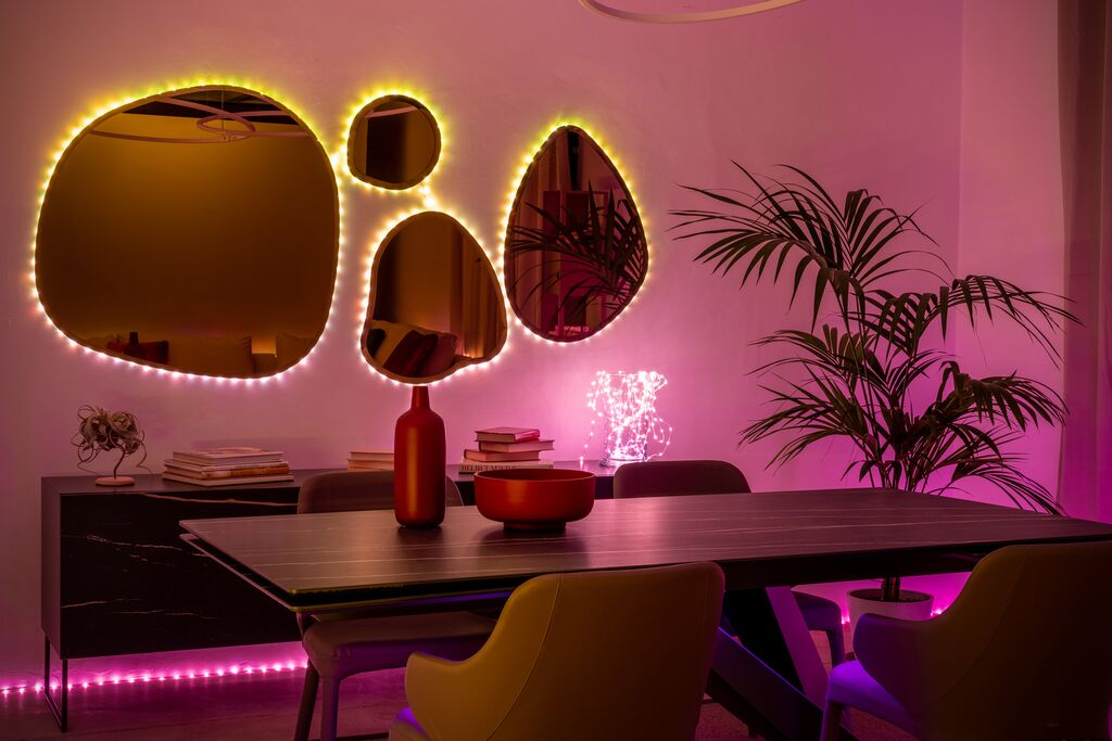Eetkamer met donkere tafel, verlichte spiegels aan de muur en roze verlichting.