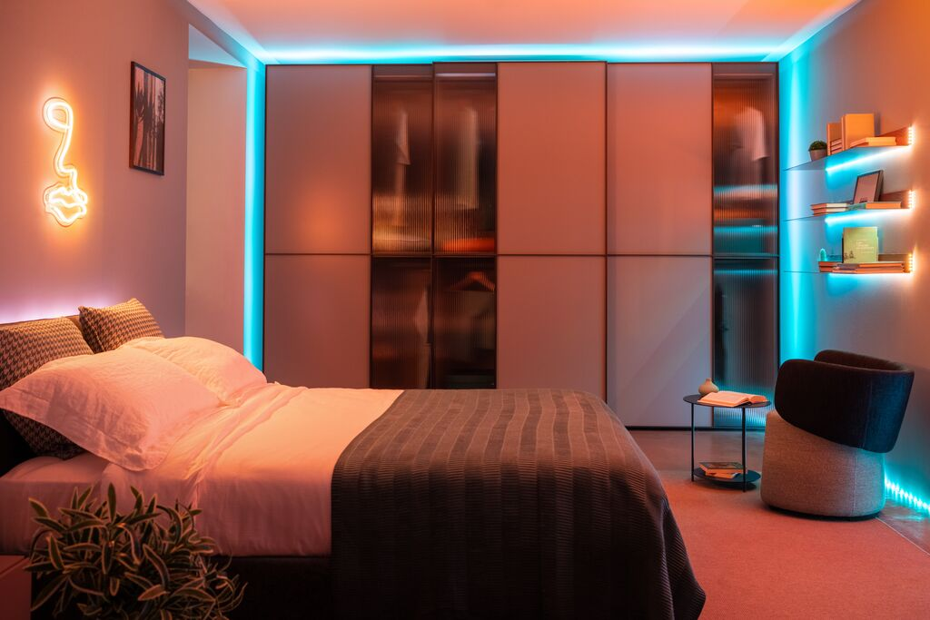 Moderne slaapkamer verlicht met oranje en blauwe LED's, met een grote kledingkast, bed en planken.