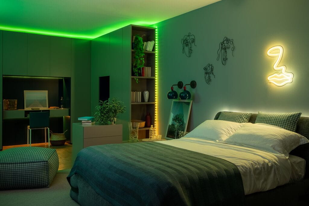 Een moderne groene slaapkamer met een tweepersoonsbed, neonverlichting, boekenplank, bureau en wandkunst.
