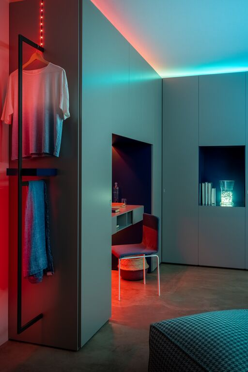 Moderne kamer met grijs meubilair, kledingrek, bureau en sfeervolle rode en turquoise LED-verlichting.