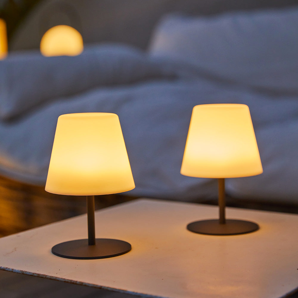 Due piccole lampade da tavolo wireless con luce gialla calda su un tavolo bianco con sfondo sfocato.