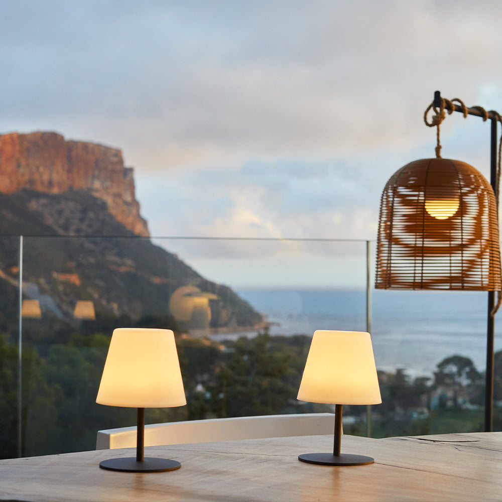 Due piccole lampade da tavolo e una lampada a sospensione su un tavolo di legno con vista sul mare e sulle scogliere.