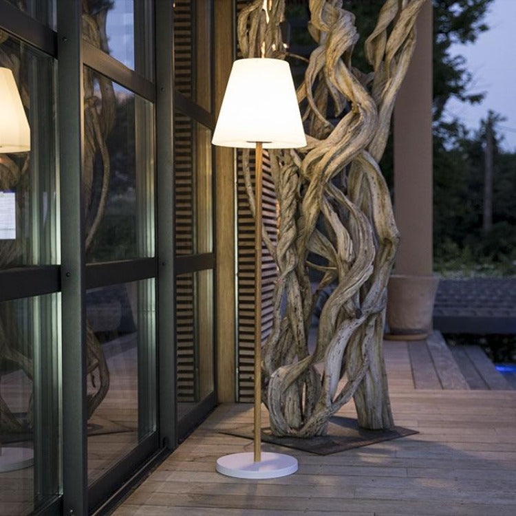 Una lampada da terra illuminata si trova su un terrazzo in legno accanto a grandi porte in vetro.
