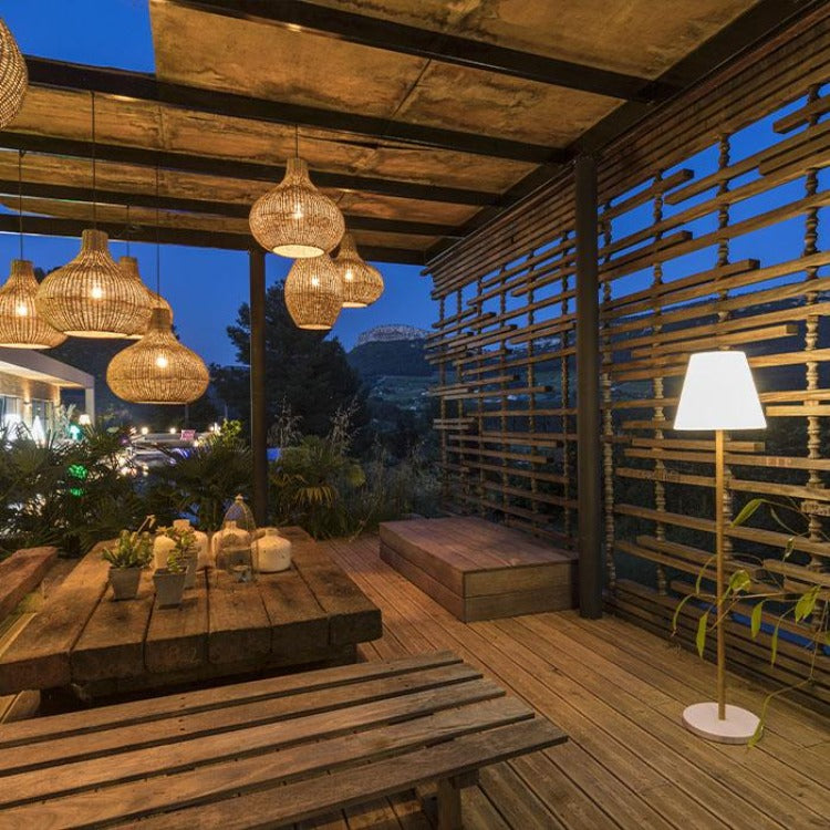 Patio in legno illuminato con tavolo da pranzo e lampade a sospensione in vimini.