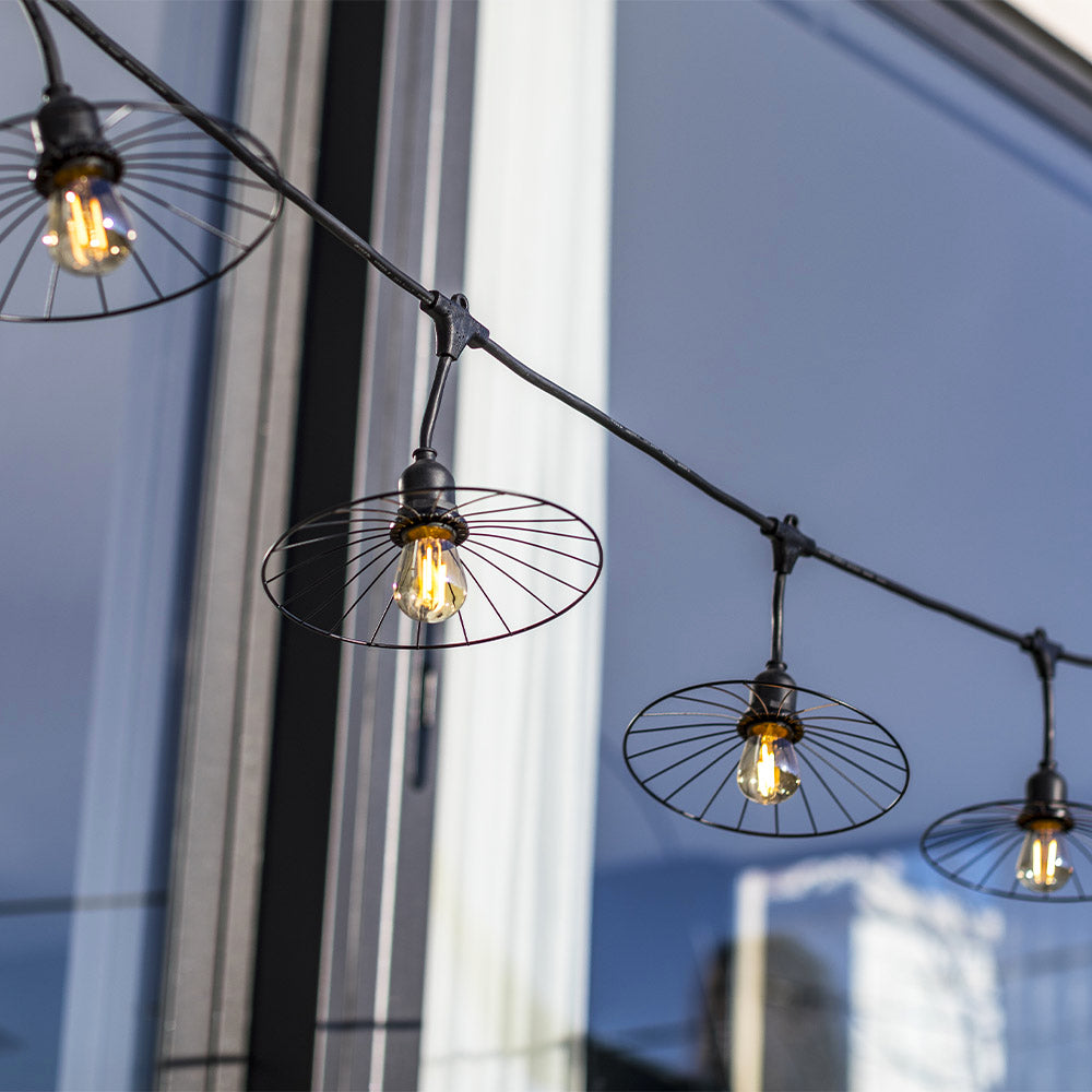 Lichterkette mit vier Glühbirnen in runden Metallschchirmen vor einem blauen Fenster.