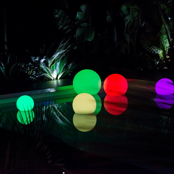 Bunte leuchtende Kugeln schwimmen nachts in einem Pool vor dunkler Vegetation.