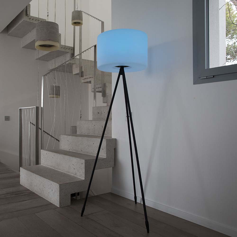 Una moderna lampada da terra a treppiede con paralume blu in una stanza luminosa con scale.