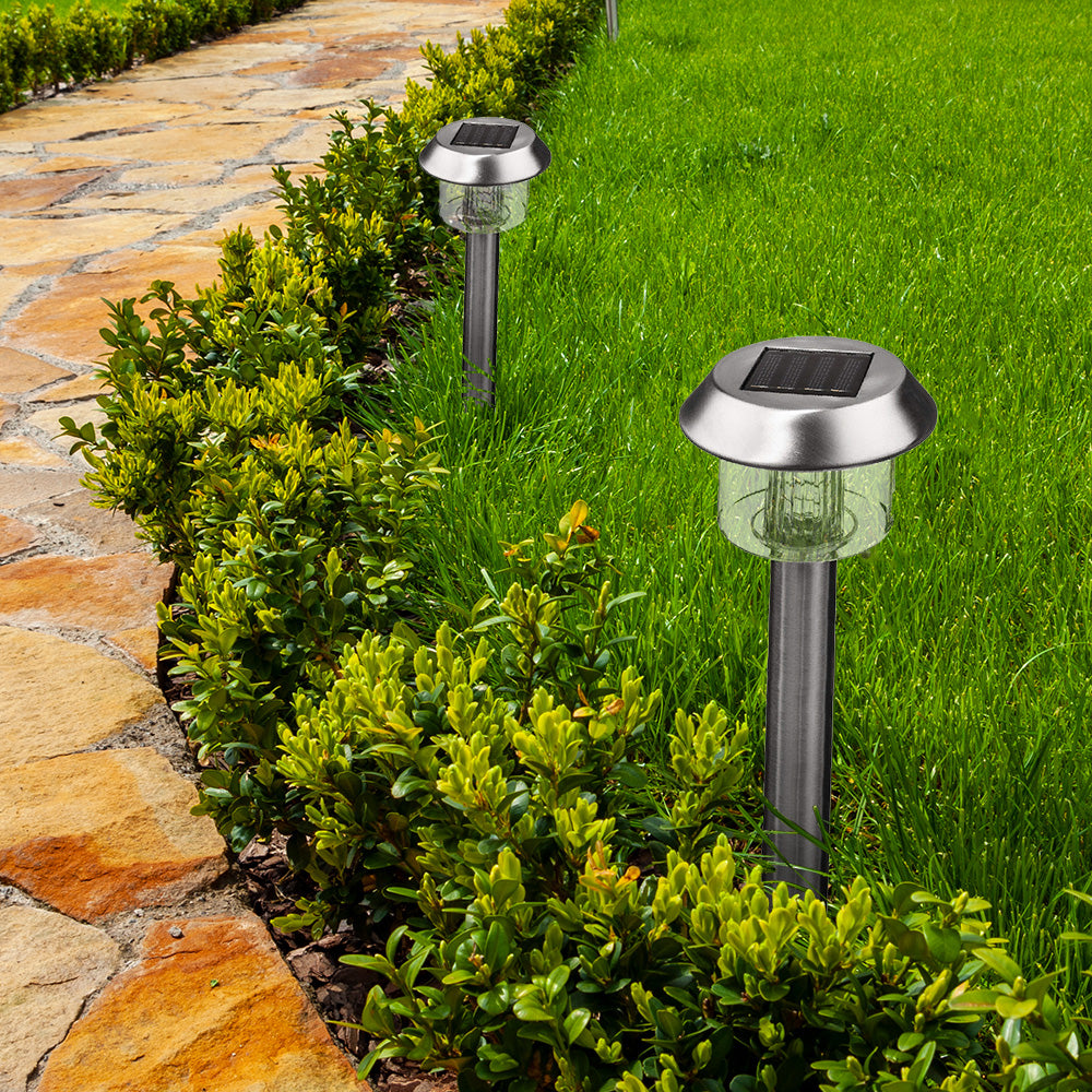 Zwei silberne Solarlampen stehen in einem grünen Garten neben einem Steinweg und Büschen.