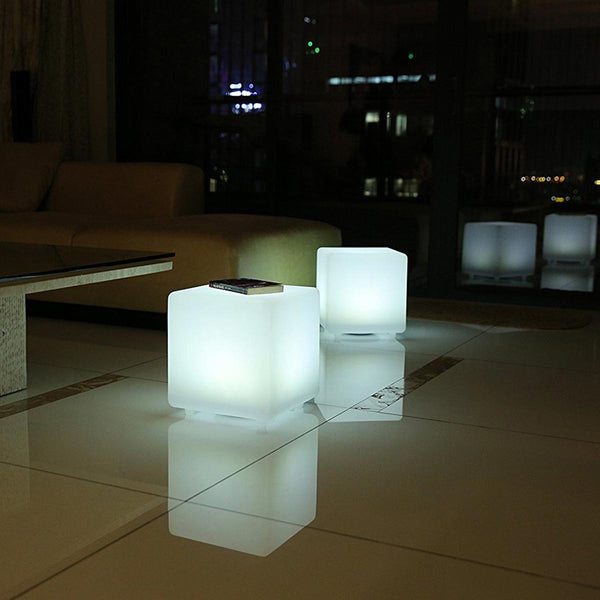 Zwei leuchtende LED-Würfel stehen auf einem hellen Fliesenboden in einem modern eingerichteten Wohnzimmer bei Nacht.