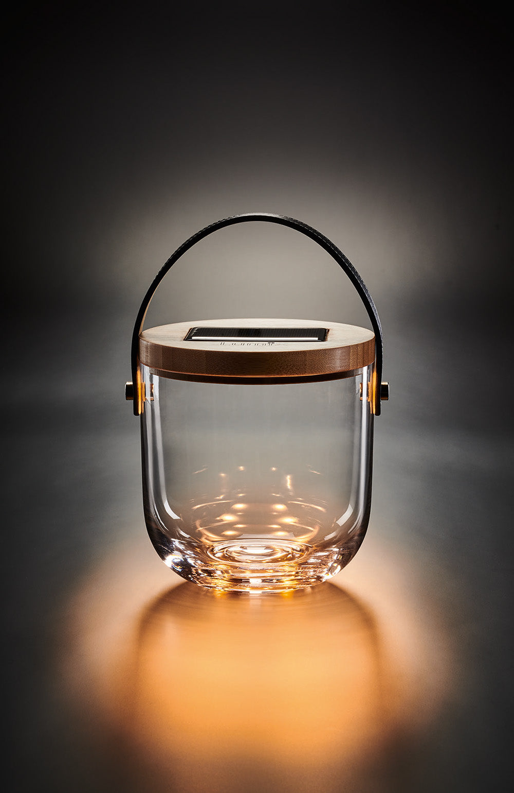 Eine elegante, zylindrische Glaslaterne mit Holzigel und schwarzem Henkel, die warmes Licht abstrahlt.