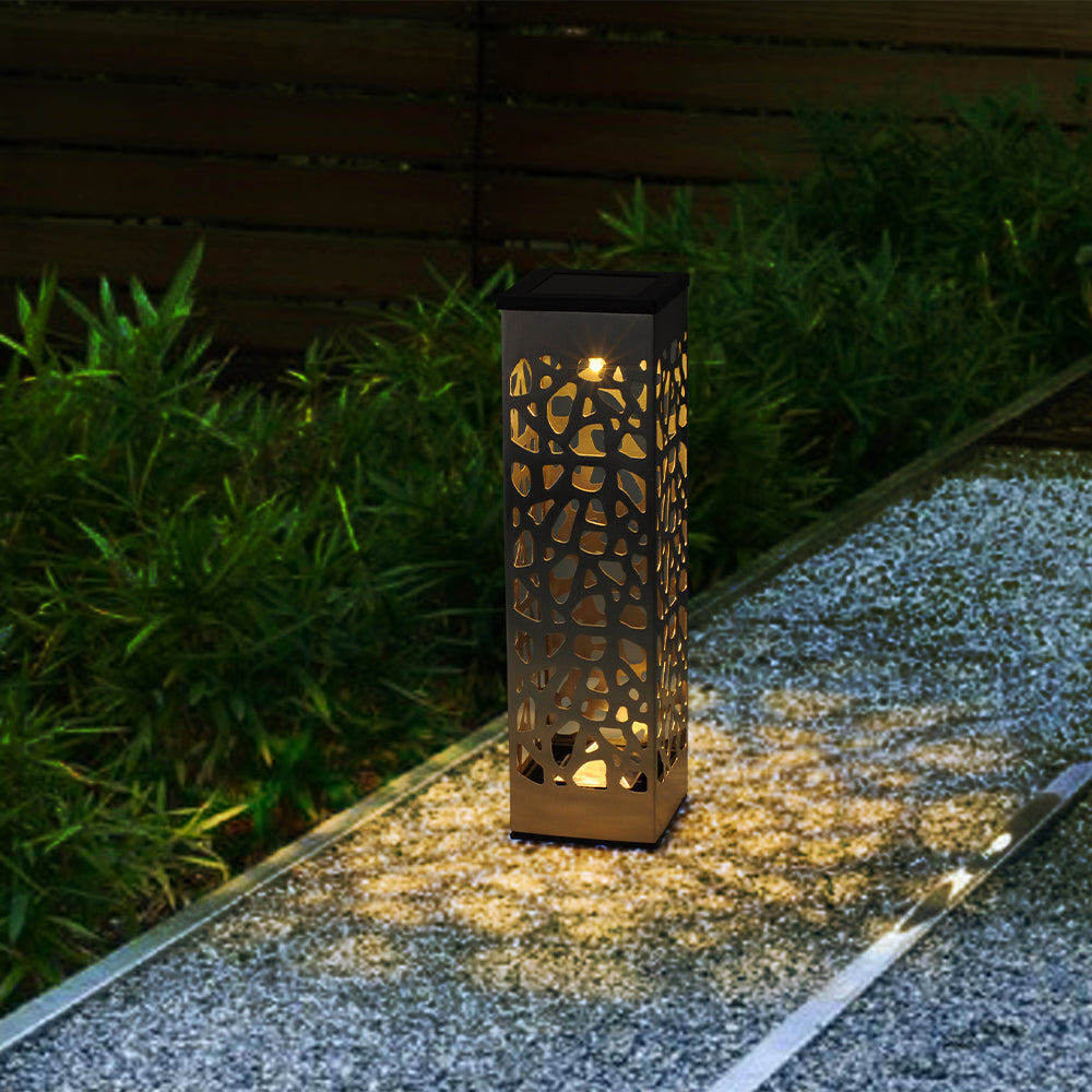Una luce solare rettangolare con motivo a rami su un sentiero da giardino vicino a piante verdi.