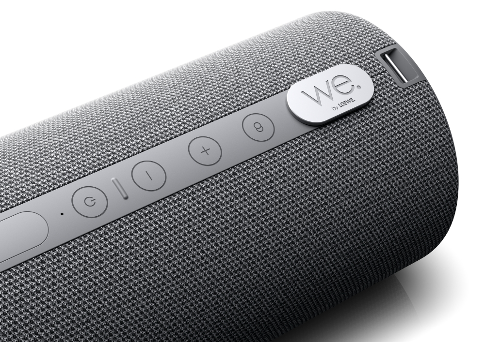 Nahaufnahme eines zylindrischen grauen Stoff-Bluetooth-Lautsprechers mit Bedienelementen und Logo.