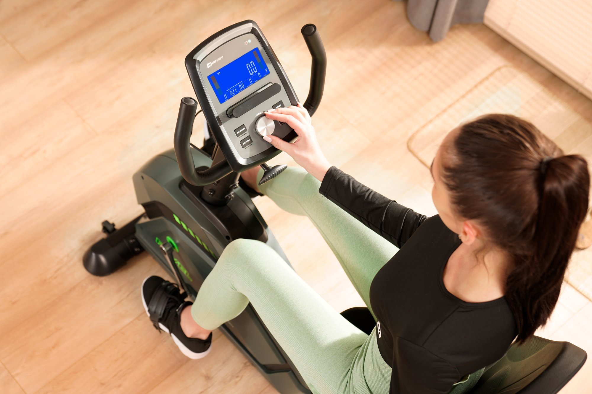 Eine Frau in Sportkleidung sitzt auf einem Heimtrainer und stellt das Display ein.