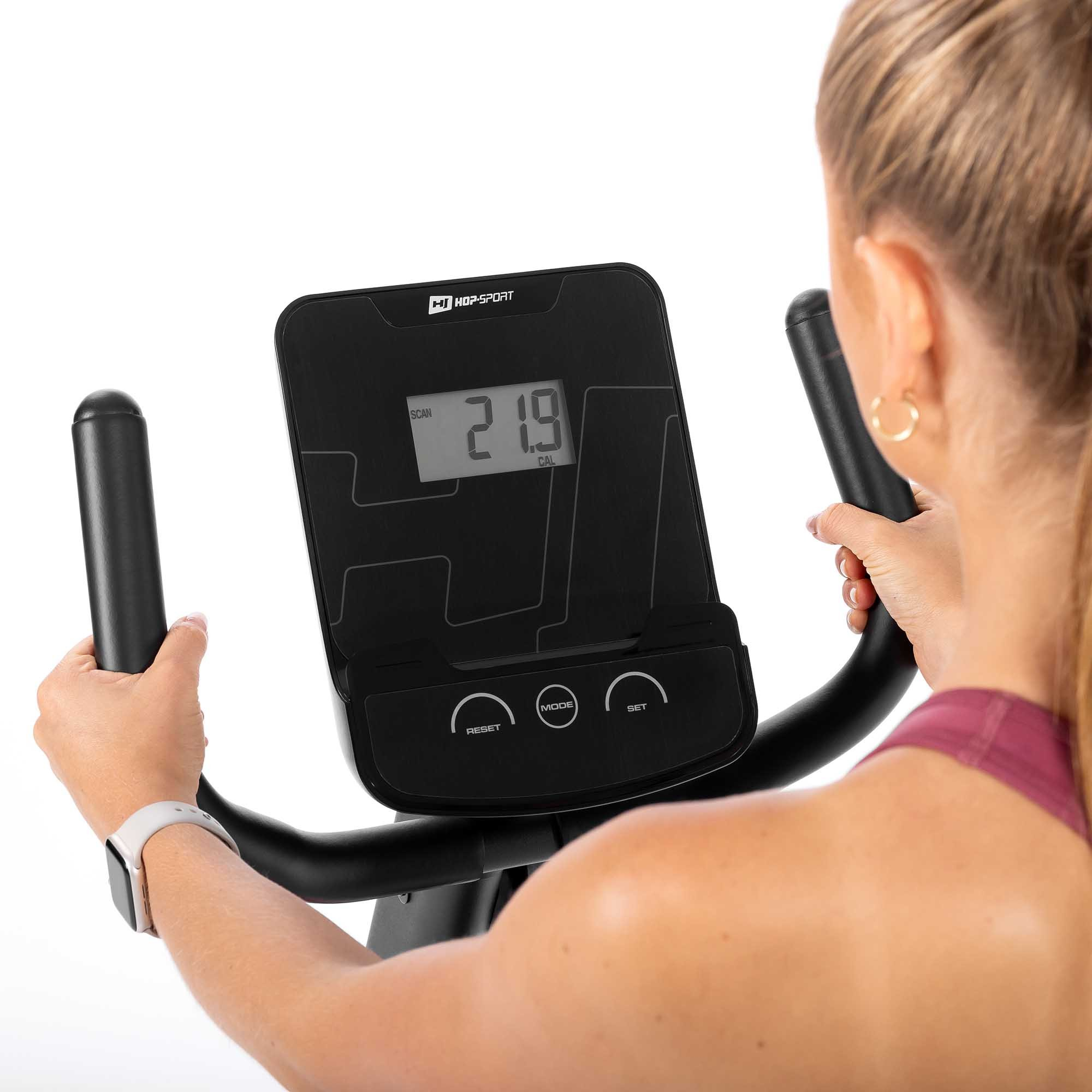 Eine Frau in Sportkleidung hält die Griffe eines Crosstrainers mit einem digitalen Display.