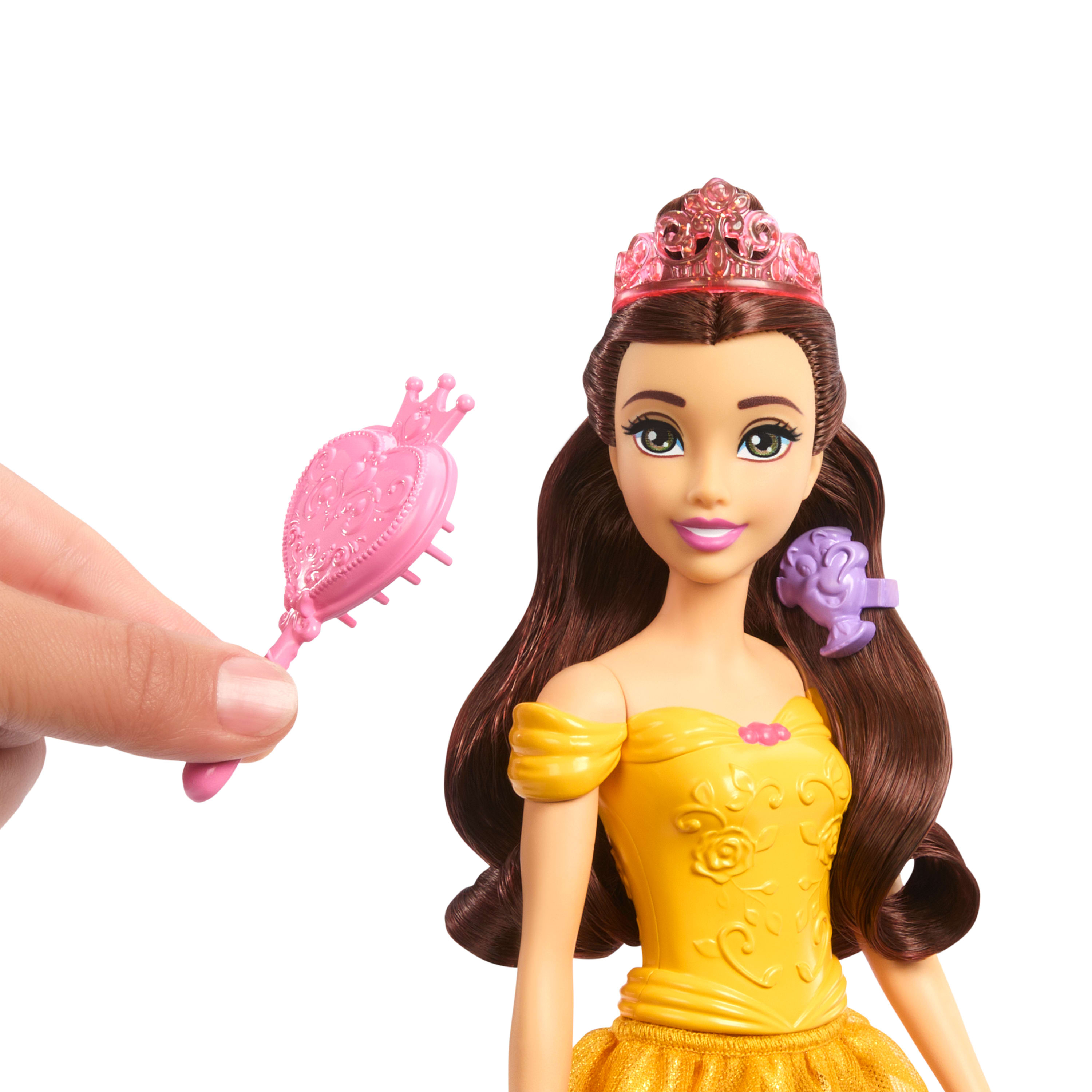 Una mano sostiene un cepillo de juguete rosa cerca de una muñeca de la princesa Bella.