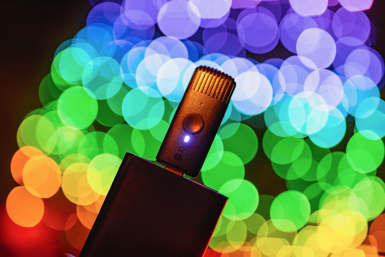 Czarne urządzenie USB z świecącą niebieską diodą LED na tle kolorowego bokeh.