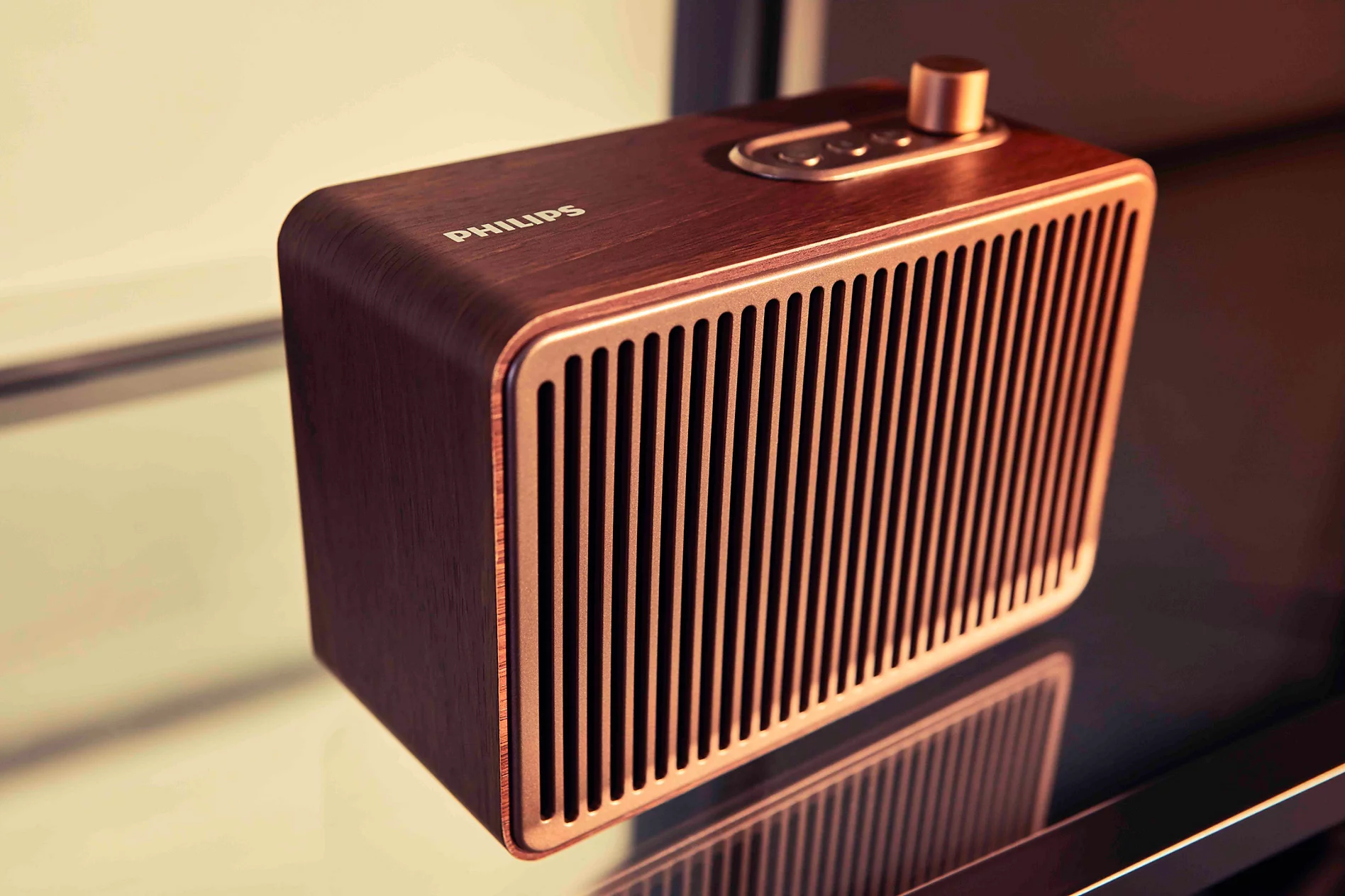 Metalik bronz ızgaralı ahşap Philips hoparlör, yansıtıcı bir yüzey üzerinde duruyor.