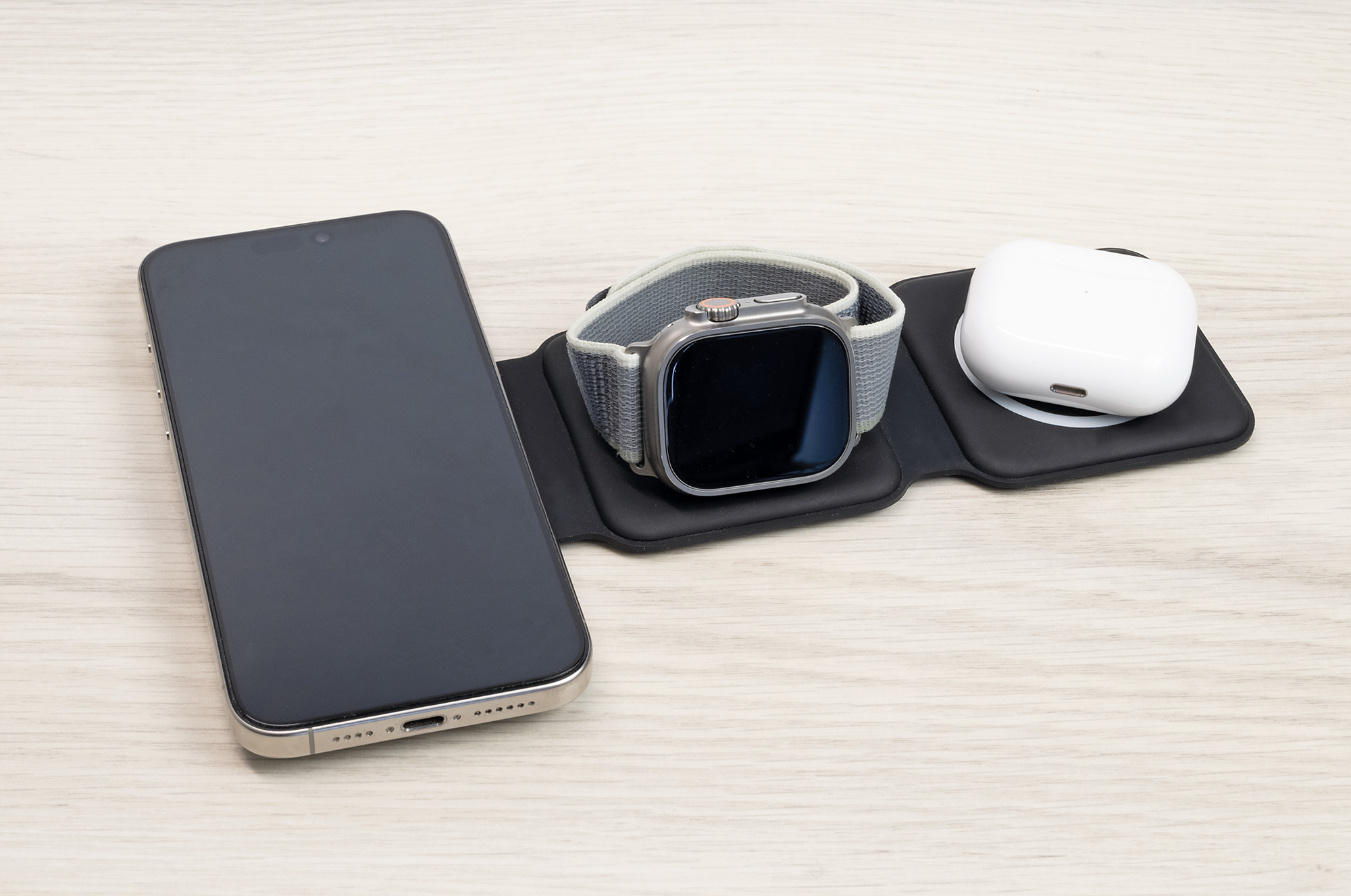 Ein Smartphone, eine Smartwatch und drahtlose Ohrhörer laden kabellos auf einer Matte auf einer Holzoberfläche.