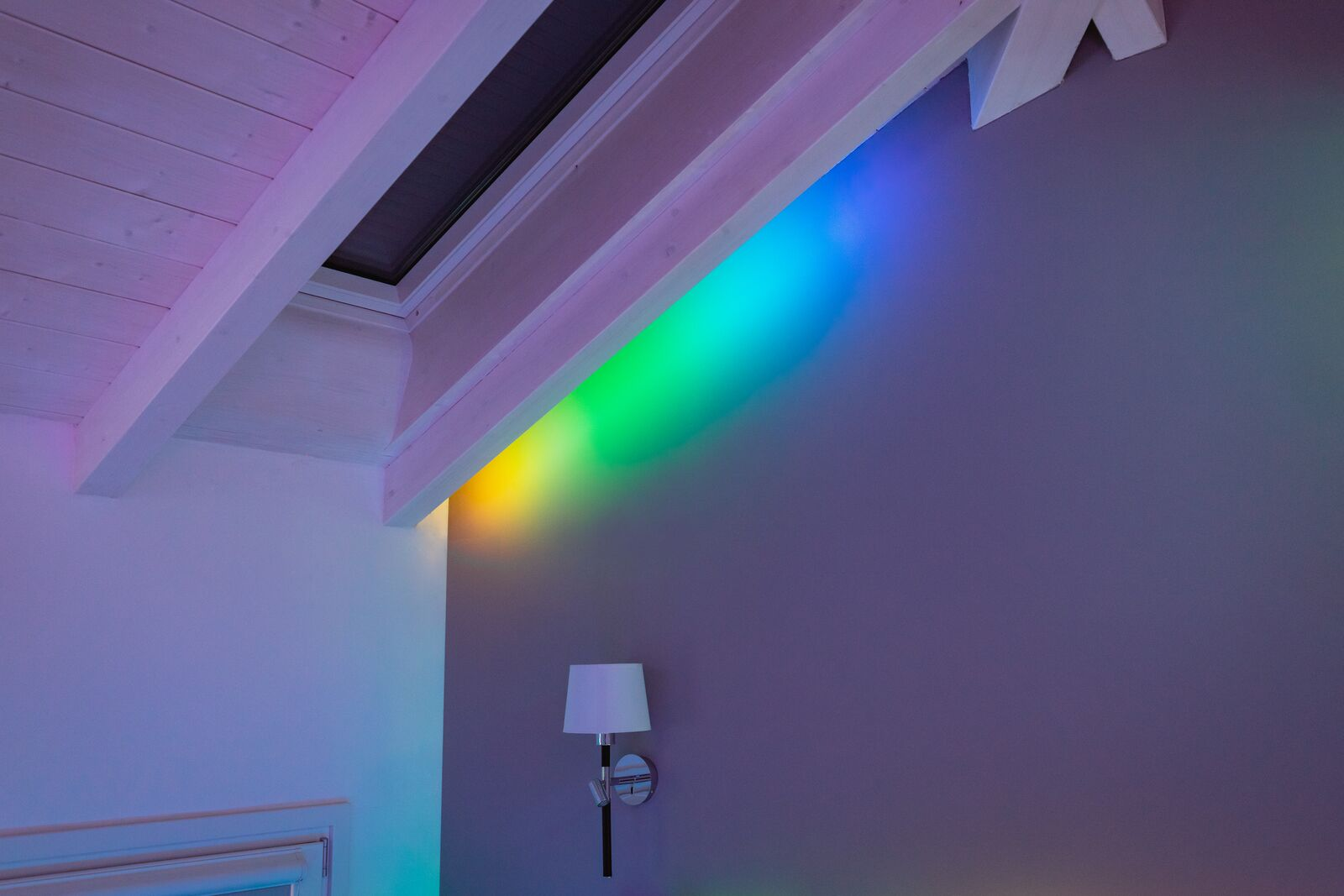 Ein Raum mit Holzbalkendecke zeigt eine Wand, die in gelbem, grünem und blauem Licht erstrahlt.