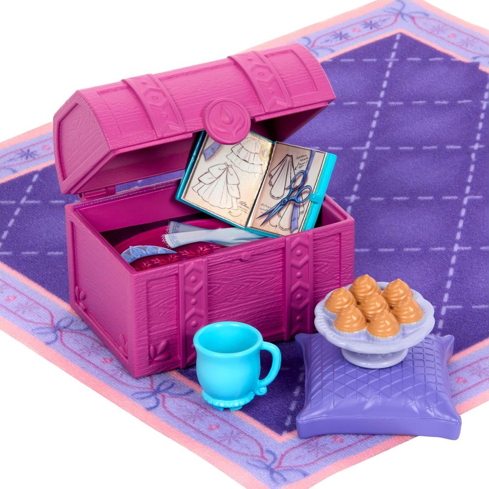 Un cofre rosa con un cuaderno de bocetos abierto, taza azul y pastelitos en un cojín sobre fondo morado.