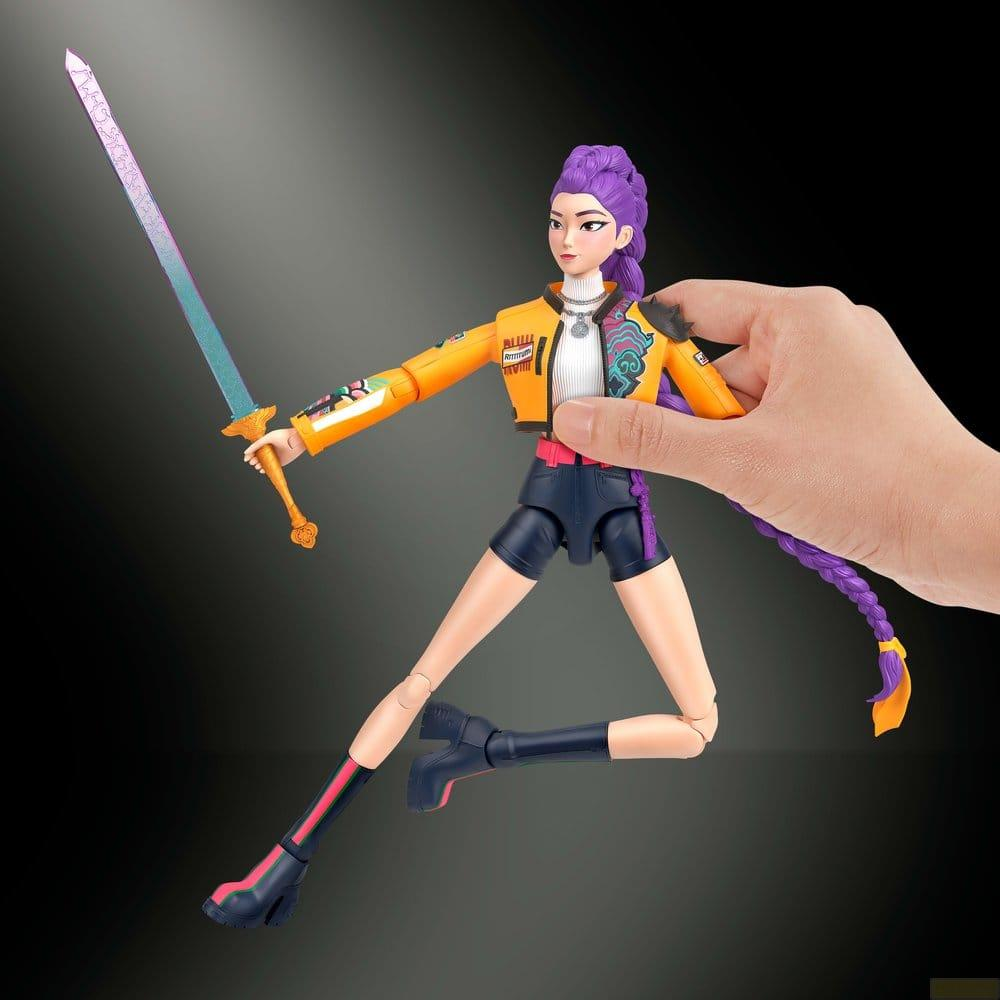 Una mano sostiene una figura de acción con pelo morado, chaqueta naranja y una espada brillante.