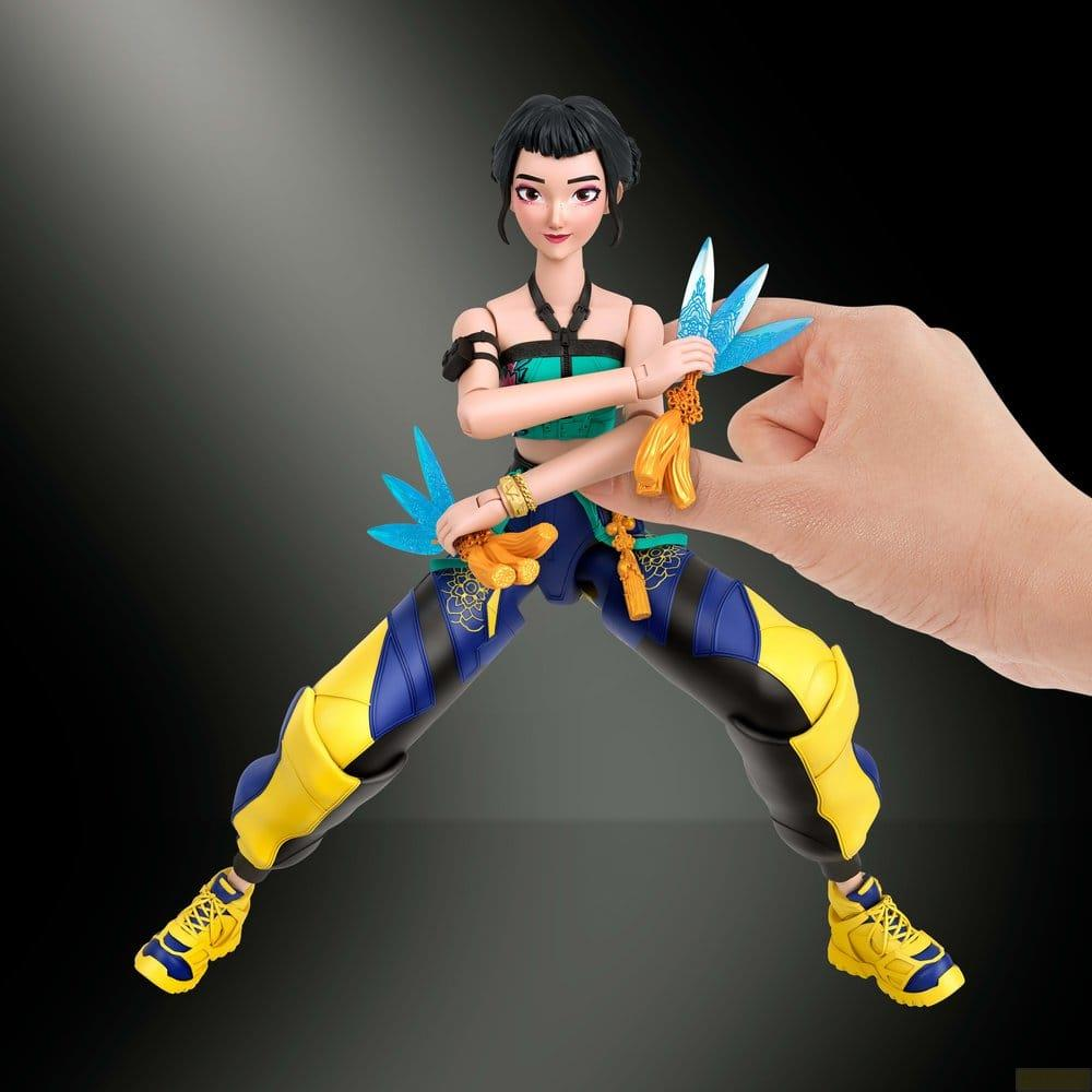 Una figura de acción asiática con cabello negro, top verde y azul, y pantalones amarillos y negros es sostenida por una mano.