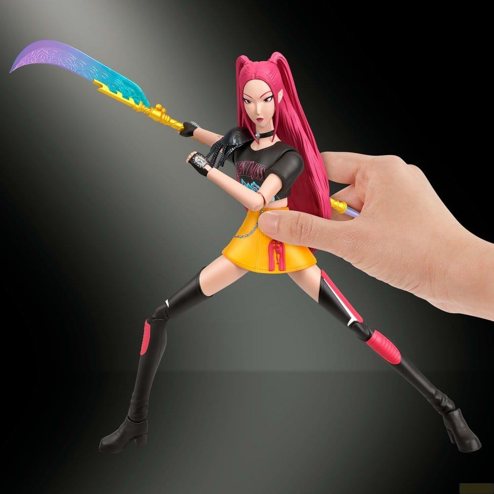 Mano sostiene una figura de acción con cabello rosa, falda amarilla y arma de hoz decorada sobre fondo negro.
