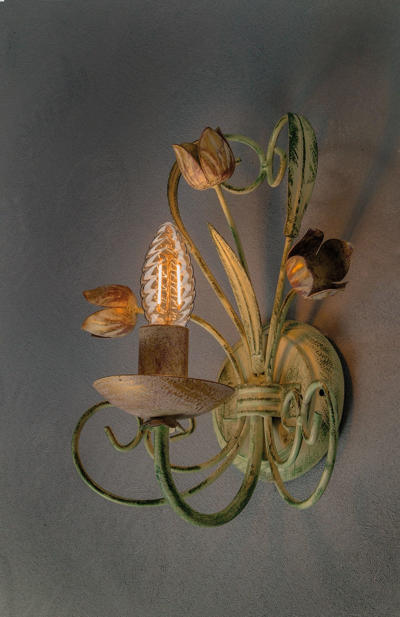 Eine dekorative Wandlampe im Blumen-Design mit glühender Glühbirne an einer grauen Wand.