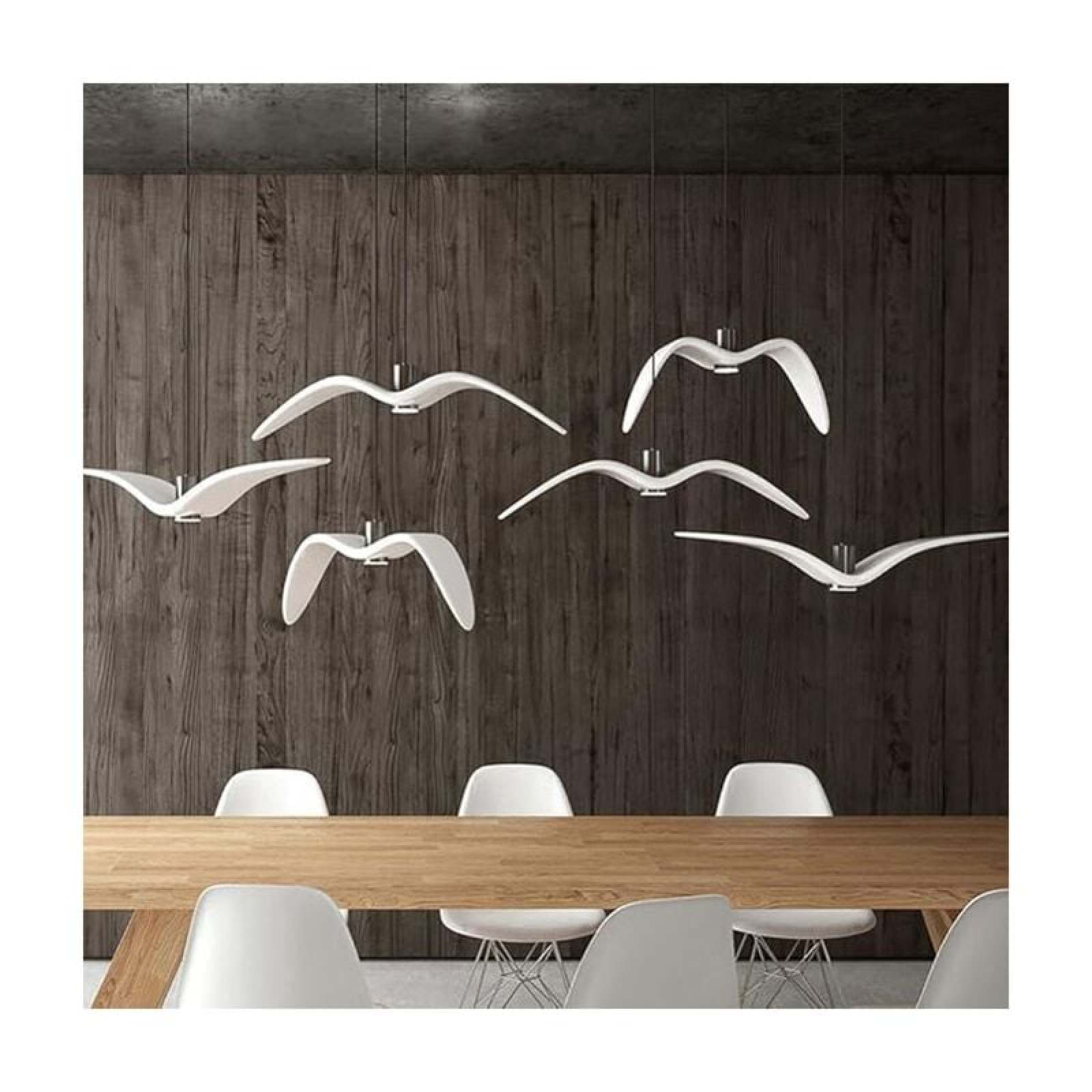 Wohnzimmer mit langem Holztisch, weißen Stühlen und fliegenden, vogelartigen Hängelampen vor Holzwand.