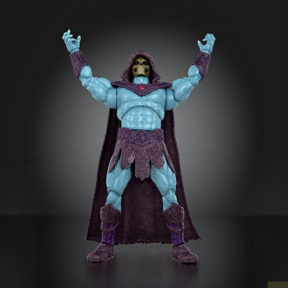 Figura de acción de Skeletor azul con capucha, capa y armadura morada, brazos levantados sobre fondo gris.