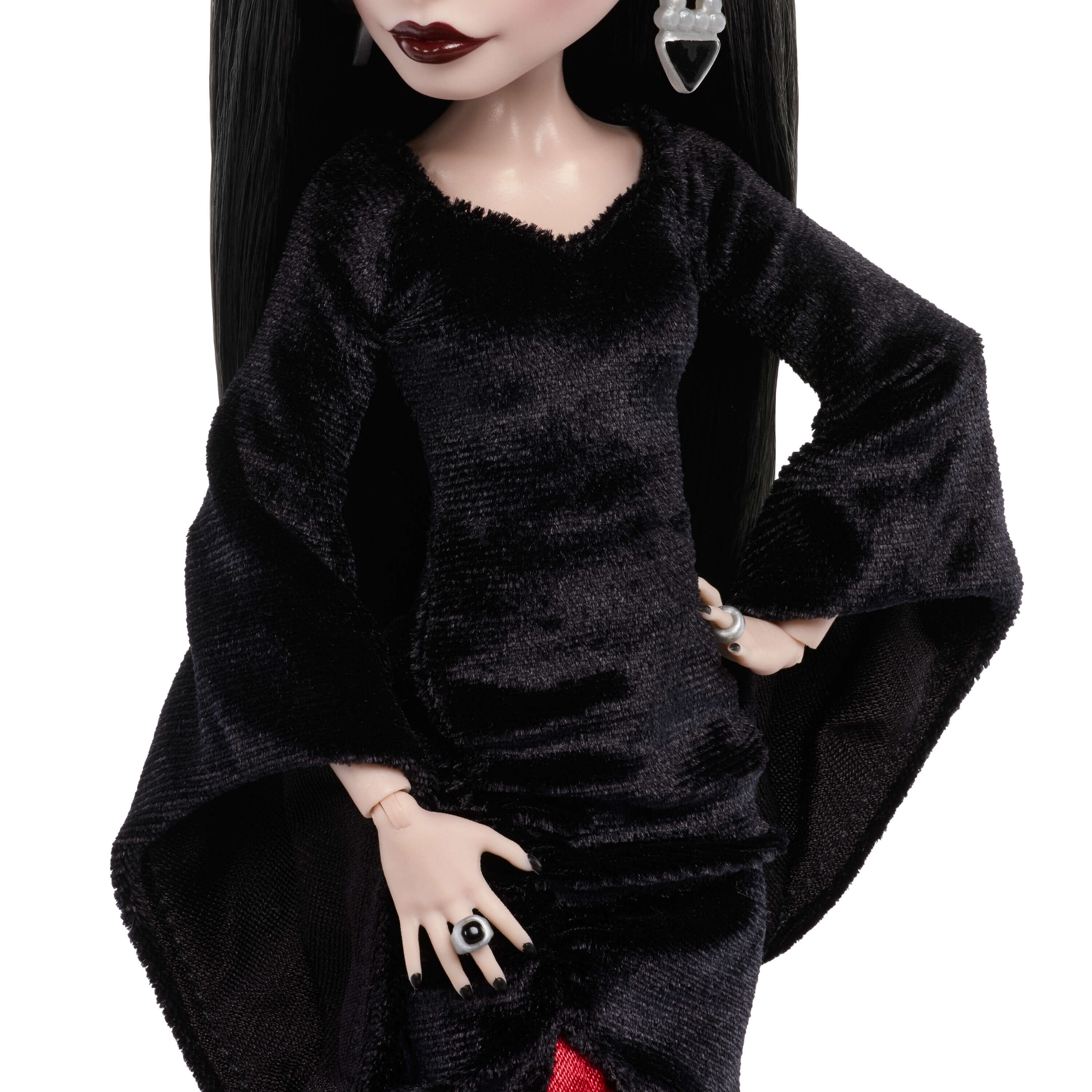 Una muñeca de moda con largo cabello negro, labios oscuros, viste un vestido de terciopelo negro con mangas acampanadas y anillos.
