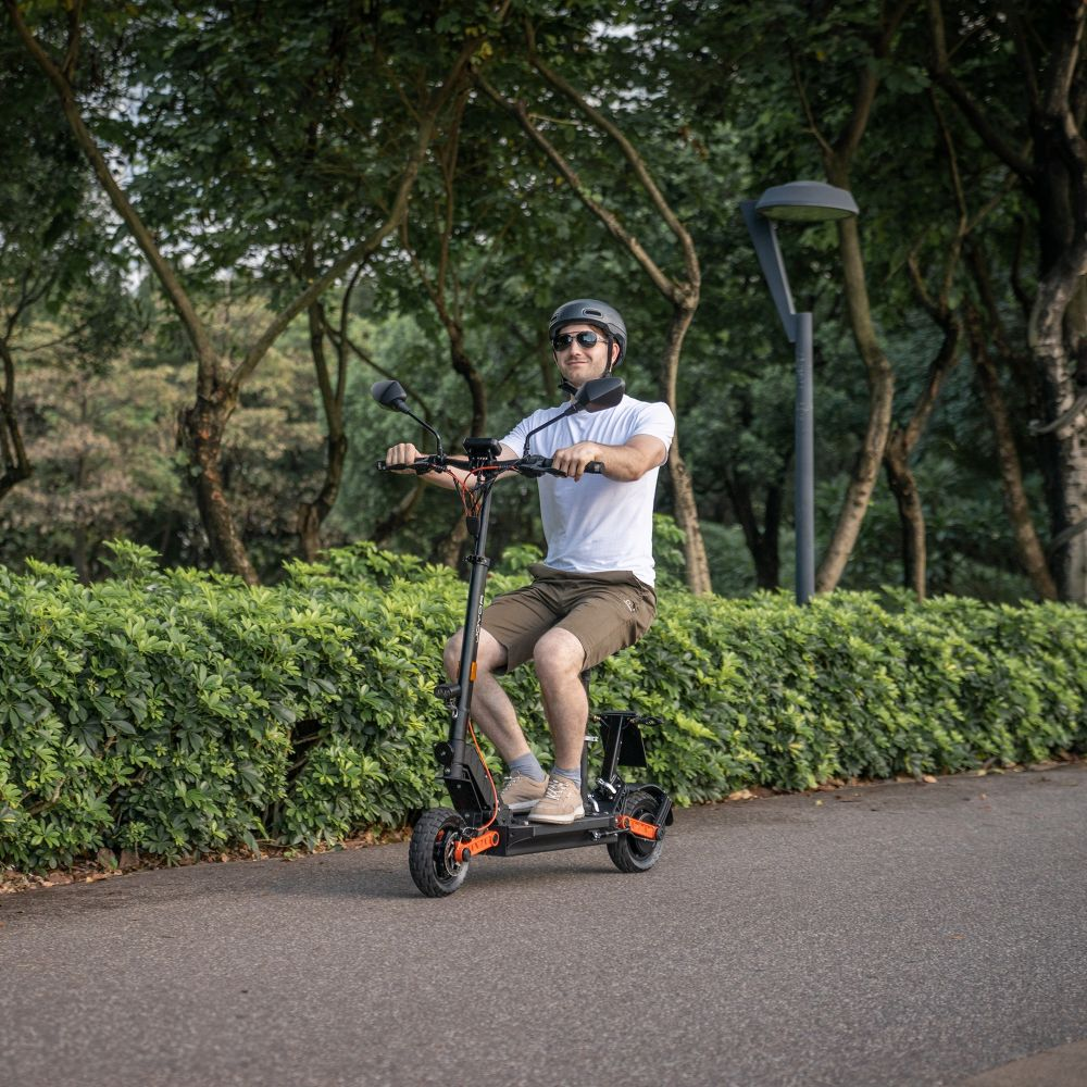 Un uomo con casco e occhiali da sole guida un monopattino elettrico su un sentiero asfaltato.
