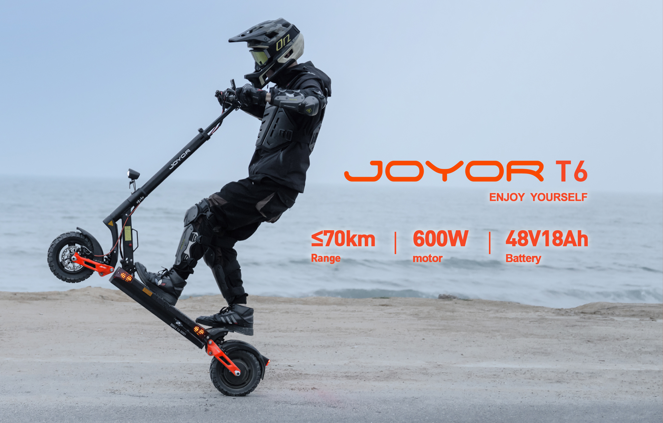 Un pilota con indumenti protettivi fa un'impennata su un monopattino elettrico nero Joyor T6.