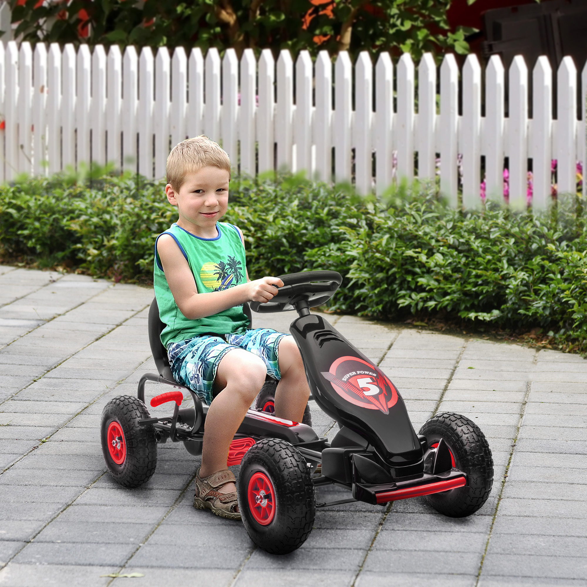 Un bambino con una canotta verde guida un go-kart nero su un sentiero lastricato davanti a un recinto bianco.