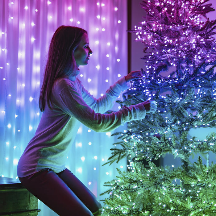 Eine Frau schmückt einen leuchtenden Weihnachtsbaum vor einer Lichterwand.