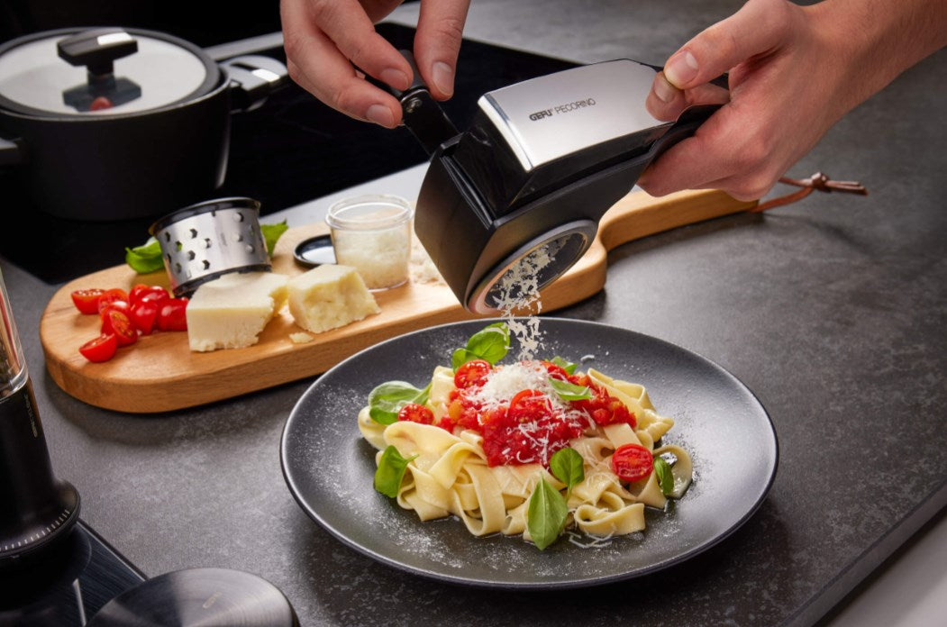 Eine Person reibt Käse auf einen Teller Pasta mit Tomatensoße und Basilikum.