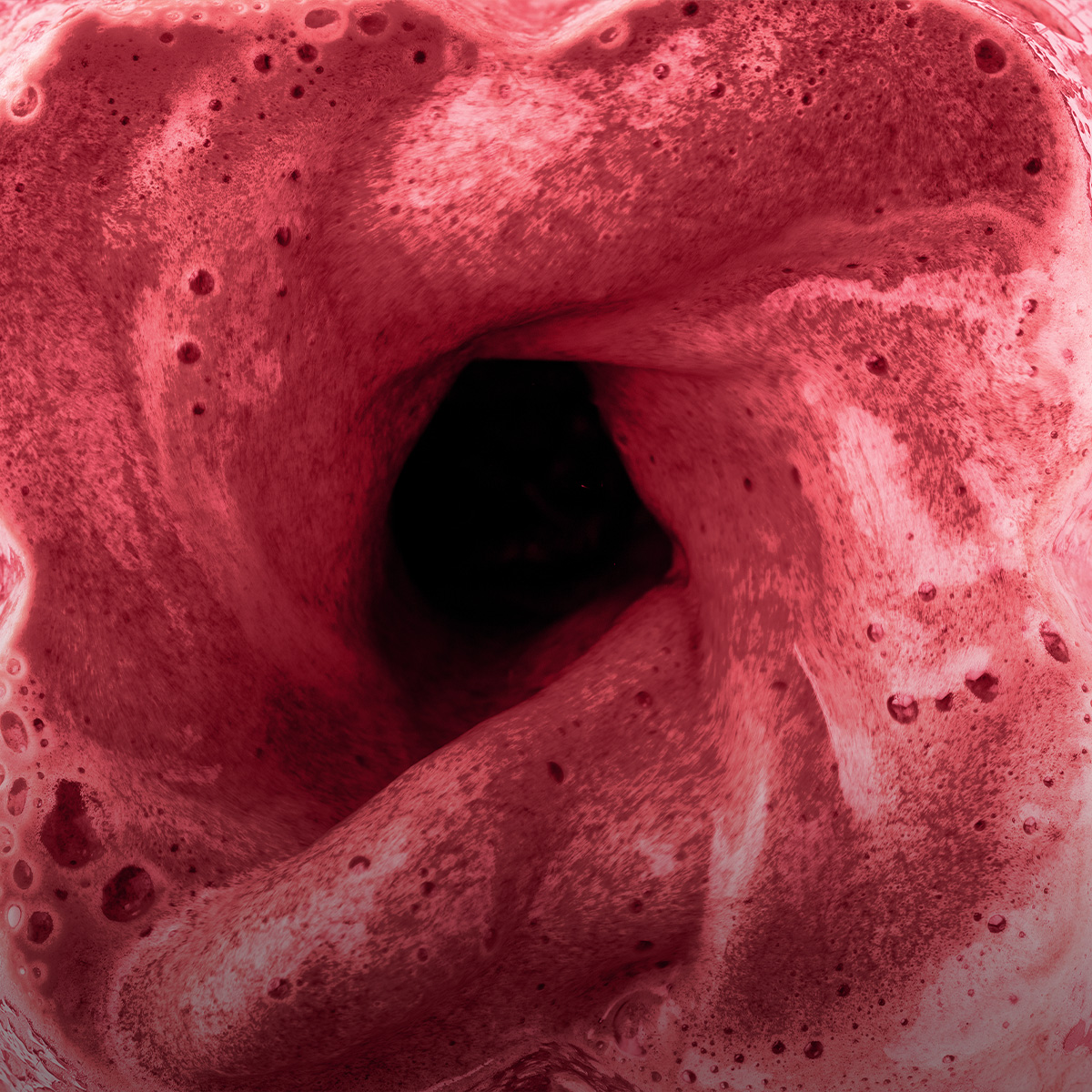 Draufsicht auf einen roten, schäumenden Smoothie in einem Mixer mit schwarzem Loch in der Mitte.