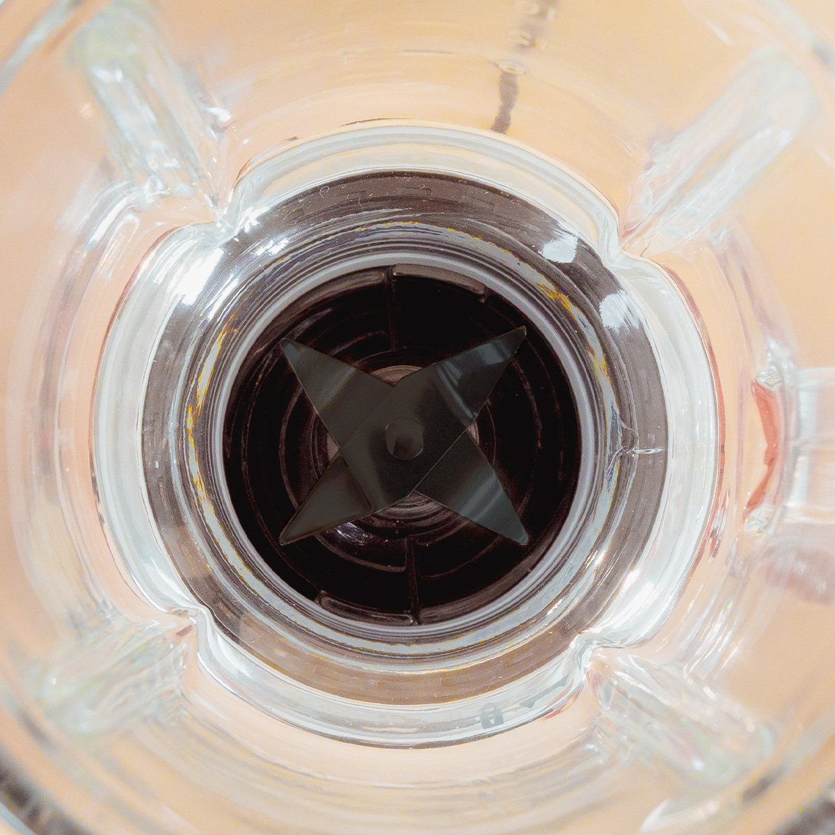 Blick von oben in ein leerer Glasmixer, fokussiert auf die dunklen vier Klingen am Boden.