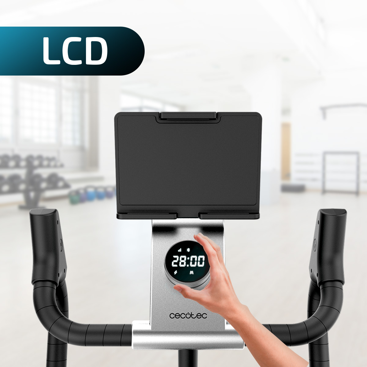 Mano che tocca lo schermo LCD rotondo di una cyclette davanti allo sfondo sfocato di una palestra.