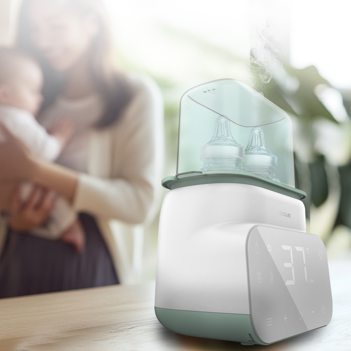 Uno sterilizzatore per biberon su un tavolo, con una madre che tiene in braccio un neonato.