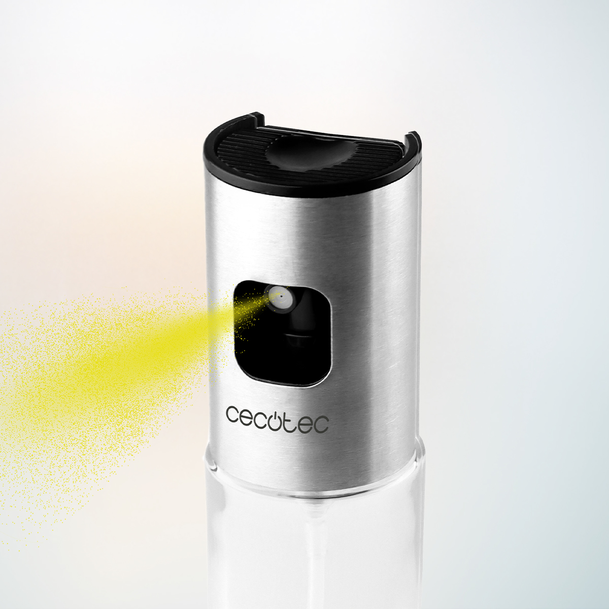 Un rociador de aceite Cecotec de acero inoxidable expulsa un fino spray amarillo.