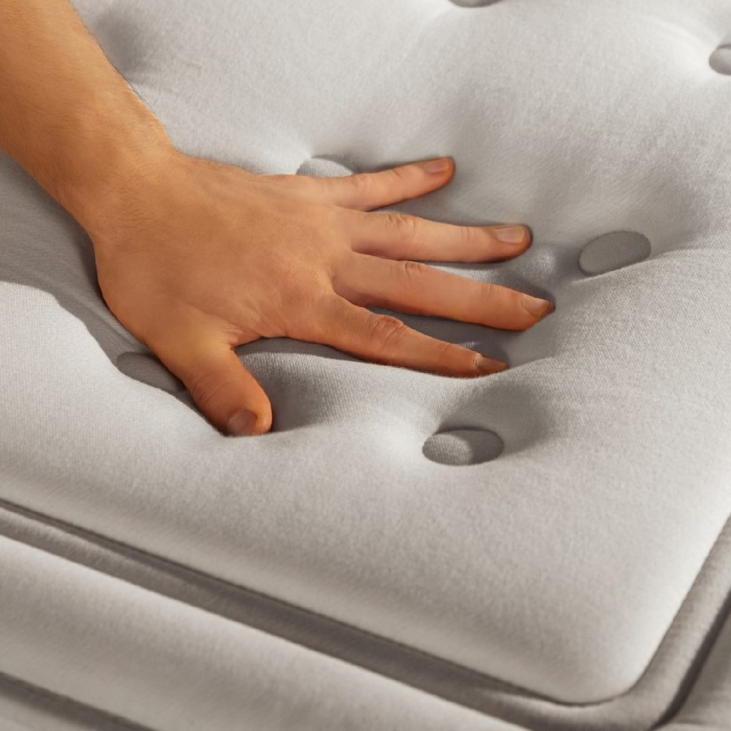 Una mano presiona un colchón gris acolchado con botones.