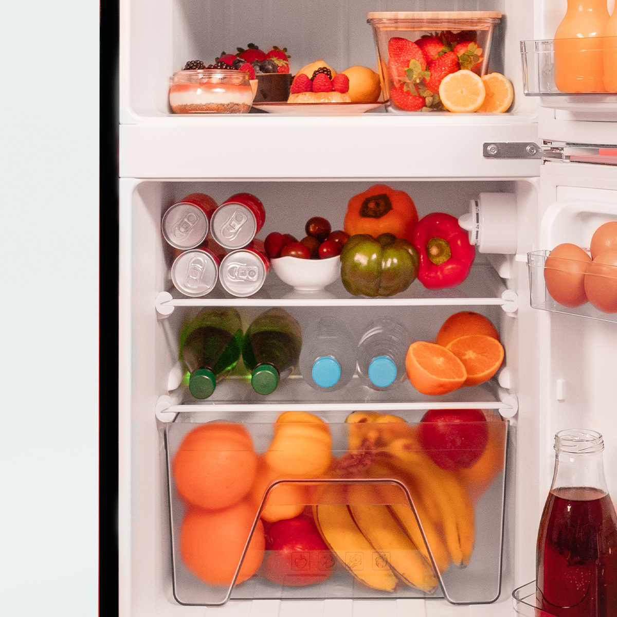 Ein offener Kühlschrank gefüllt mit frischem Obst, Gemüse, Getränkedosen, Flaschen und Eiern.