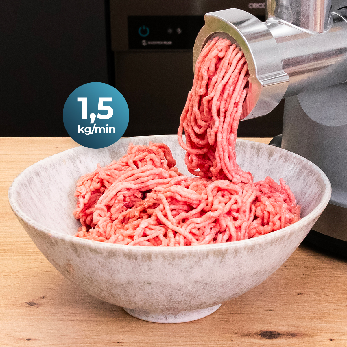 Carne macinata fresca esce da un tritacarne in una ciotola chiara su un tavolo di legno.