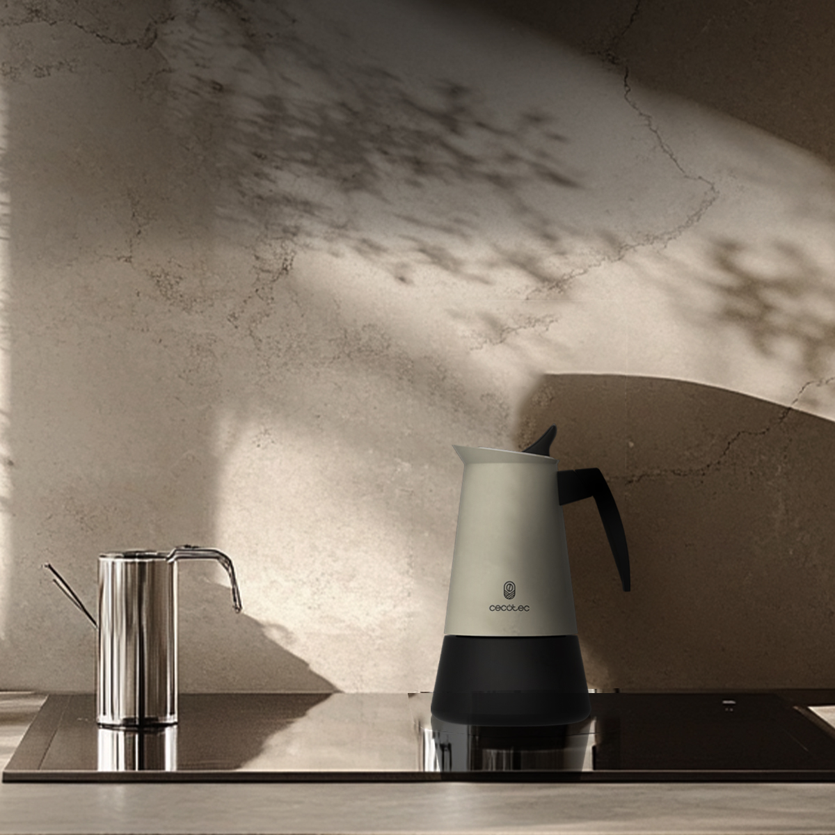 Una cafetera beige con base y asa negras se encuentra en una estufa contra una pared texturizada.