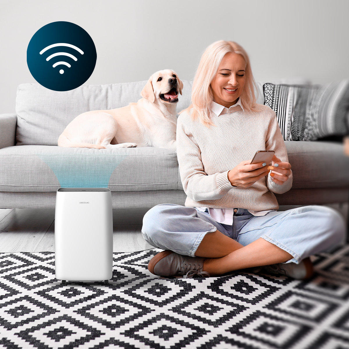 Una donna sorridente usa il telefono su un tappeto vicino a un depuratore d'aria, con un cane sul divano.